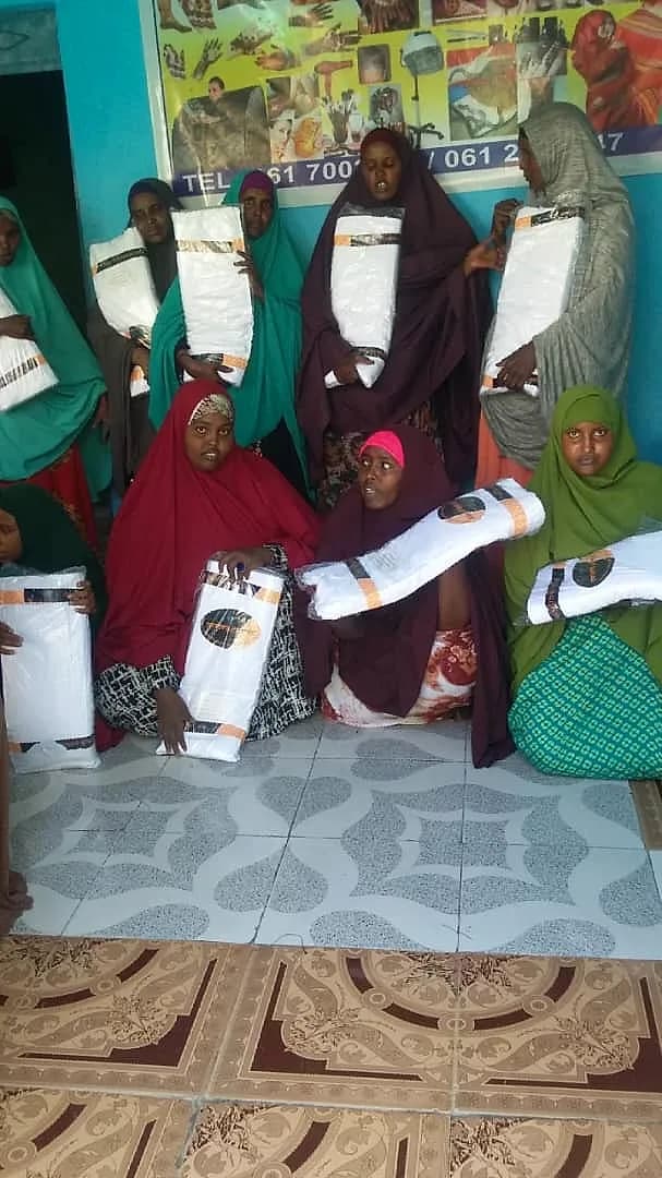 A group of RTVTI trainees in headscarves, each holding a wrapped white package, in the training room